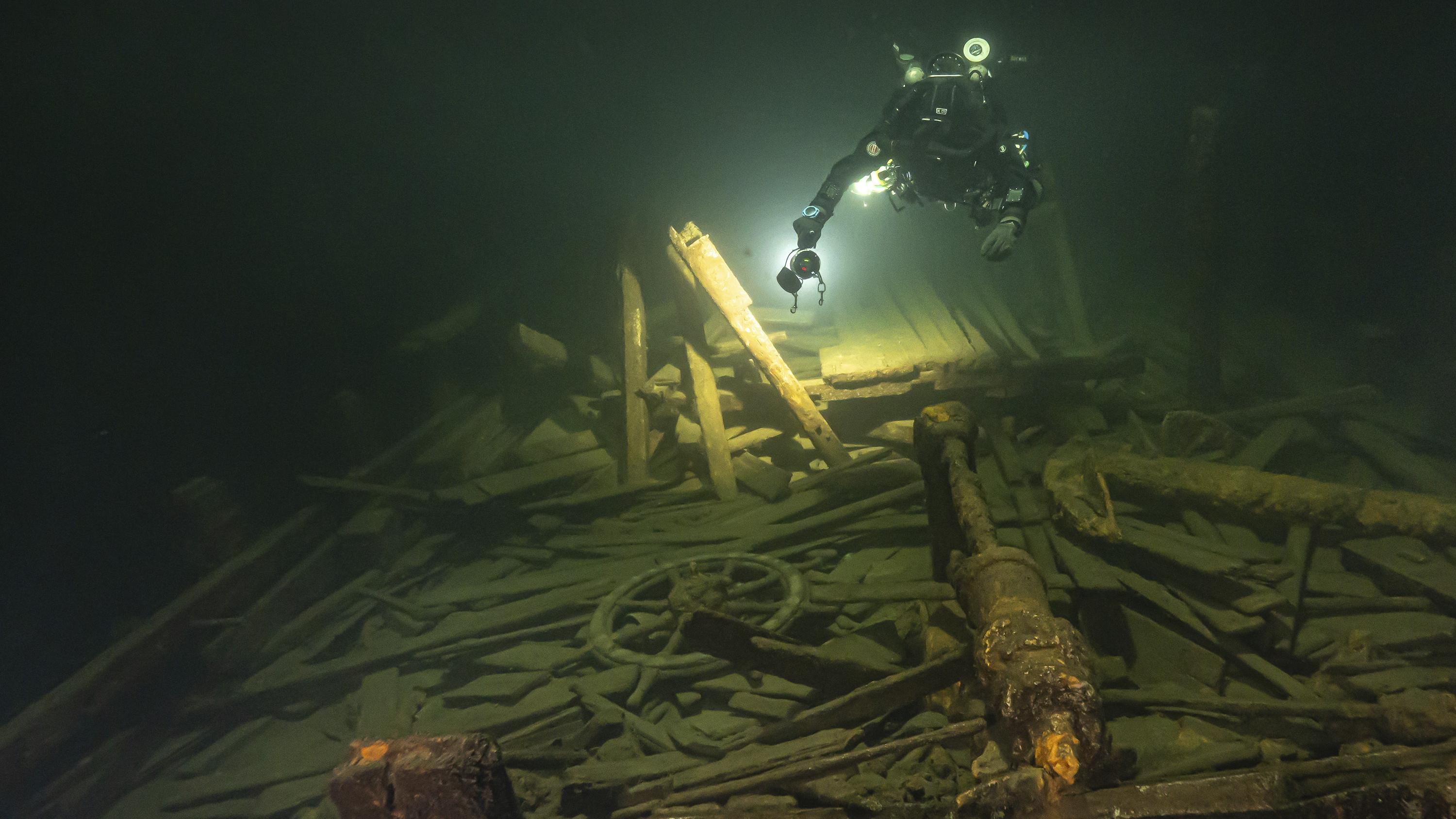 A diver uses a light to inspect wreckage of a 19th century sailing ship.