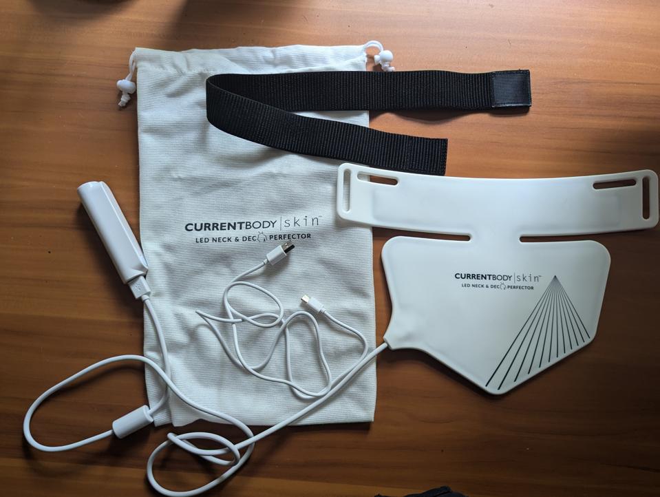 CurrentBody Skin LED Neck And Décolletage Perfector and accessories against wooden surface
