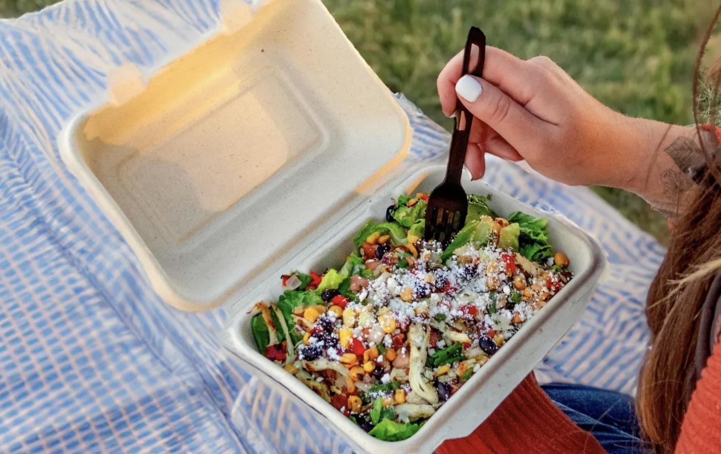 A person eats a salad from a compostable container.
