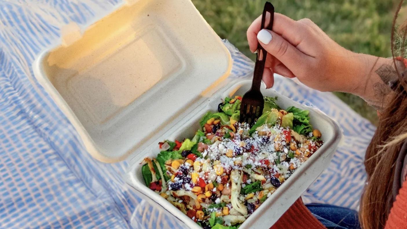 A person eats a salad from a compostable container.