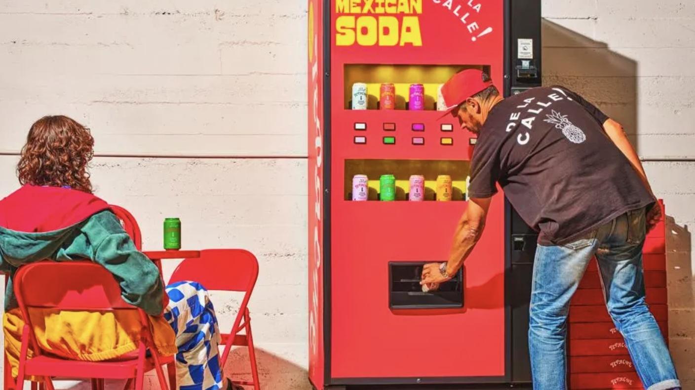 A man reaches into a De La Calle vending machine that offers Modern Mexican Soda.