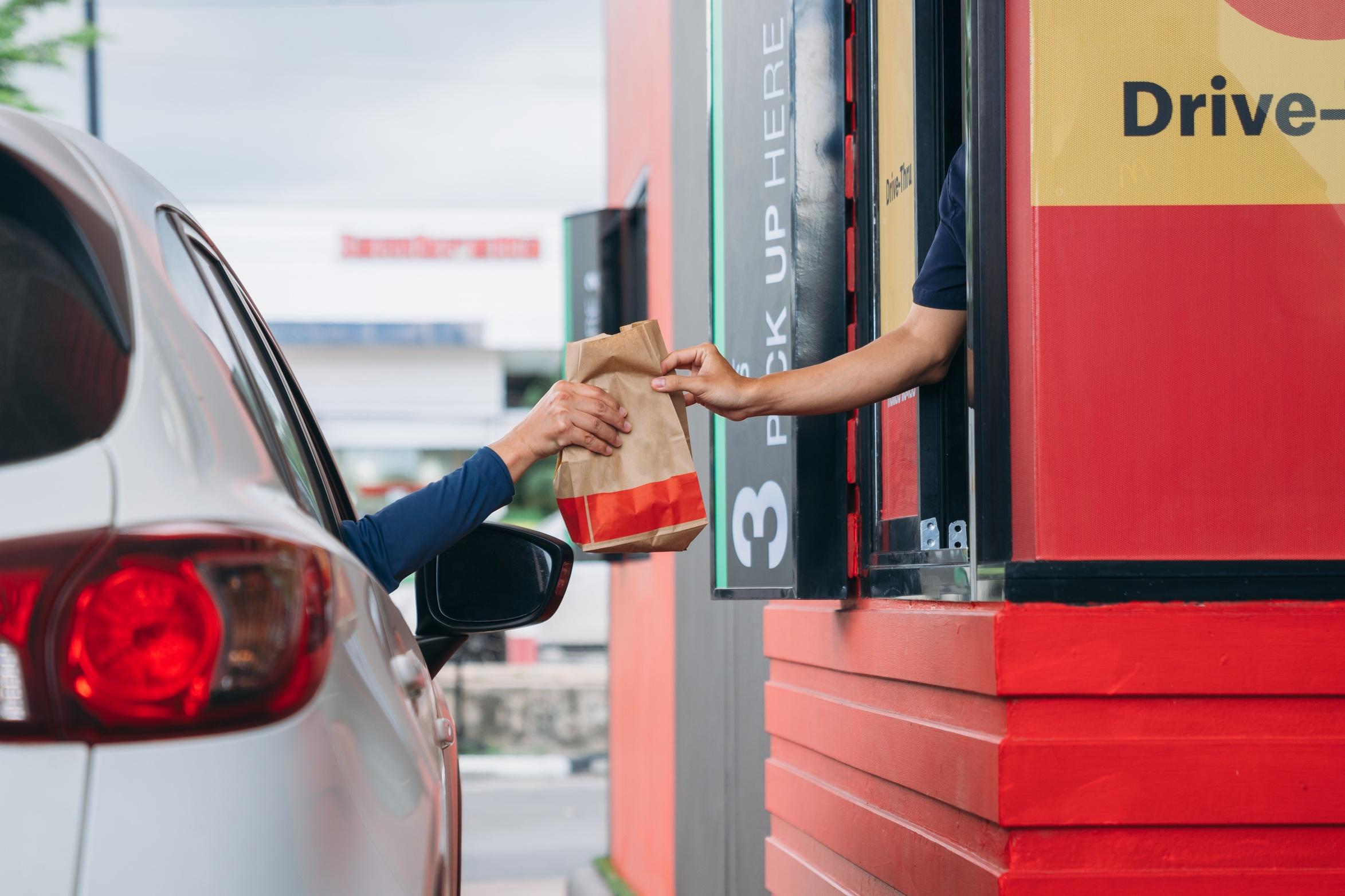 An arm extends from a white vehicle to receive a bag of food from a drive thru.