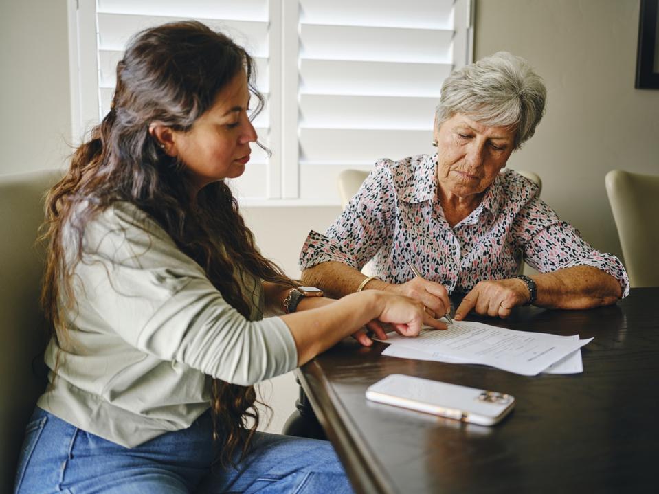 An adult daughter helps elderly mother sign document