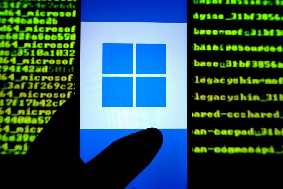 Microsoft Windows logo, in blue, on a smartphone screen in font of an image displaying green computer code.