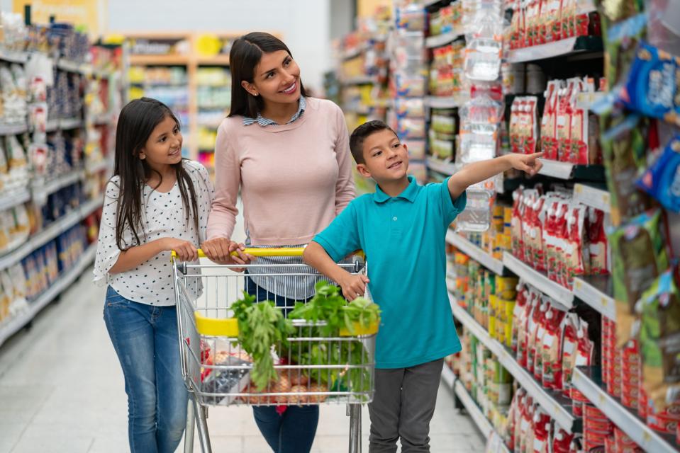 Latin american single parent with her two kids at the supermarket shopping for groceries and boy pointing at something