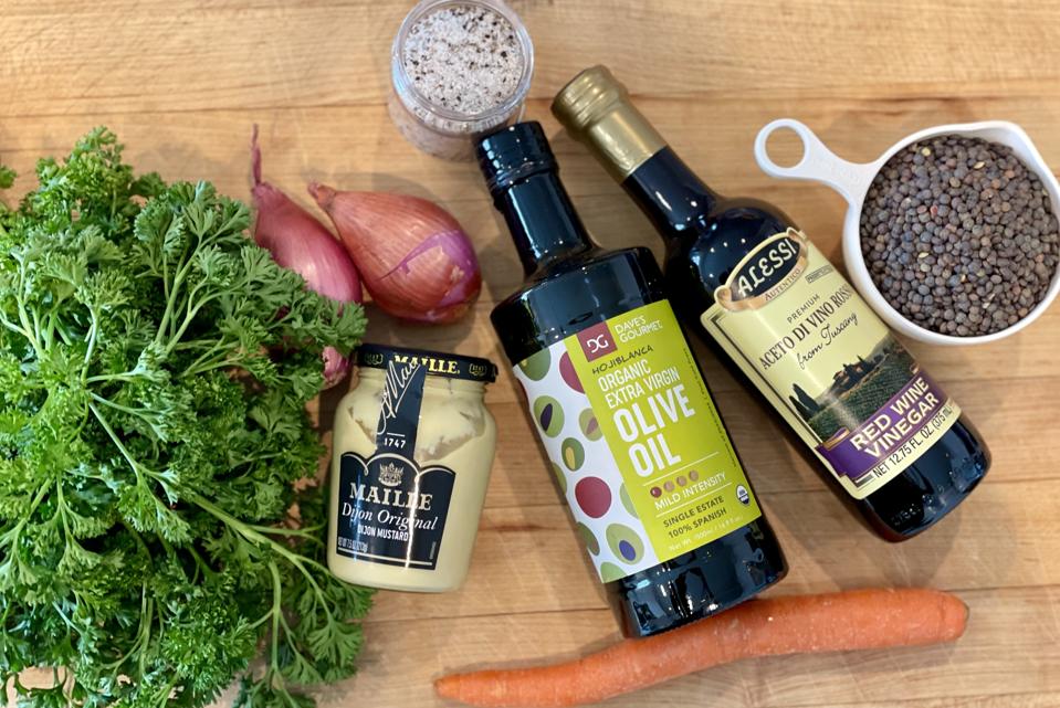 A classic vinaigrette made with red wine vinegar and Dijon mustard is all you need to flavor the warm cooked lentils. Raw orange carrots, purple shallots and green parsley add color and freshness to the salad.  In this photograph by Elizabeth Karmel are the ingredients you need to make the  French Lentil Salad; from left to right, curly parsley, shallots, Dijon Mustard, one carrot, extra-virgin olive oil red wine vinegar, salt and pepper and lentils du Puy.