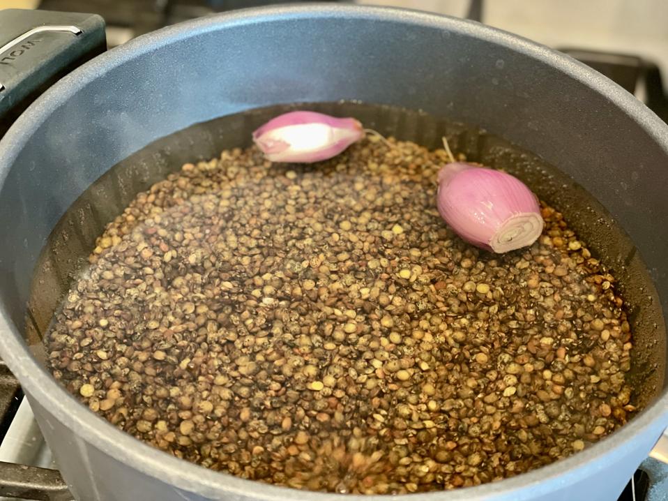 The lentils are cooked in water that is scented with a couple of whole shallots. In this photograph by Elizabeth Karmel is a pot filled with water, a cup of lentil du Puy and 2 whole shallots that have been skinned and trimmed.