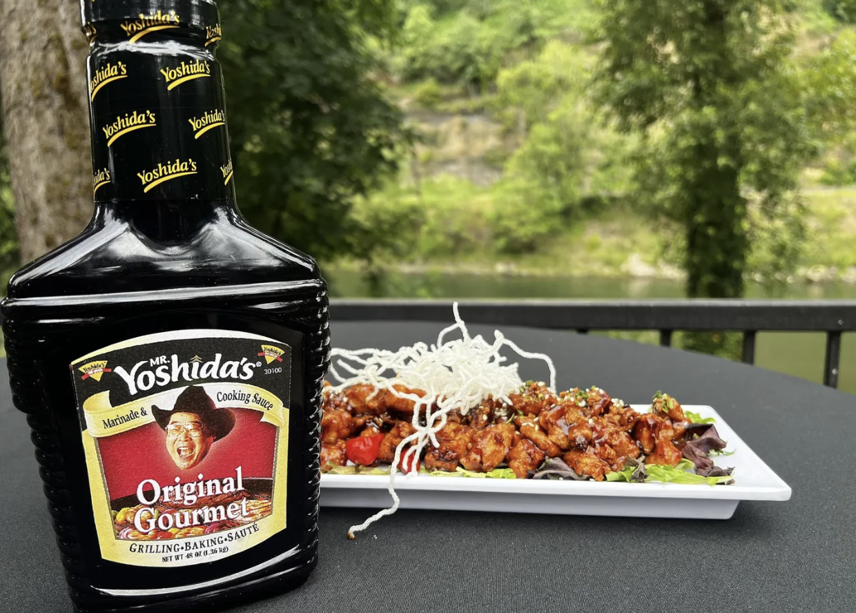 A photo shows a bottle of Mr. Yoshida's sauce next to a plate of food outdoors.