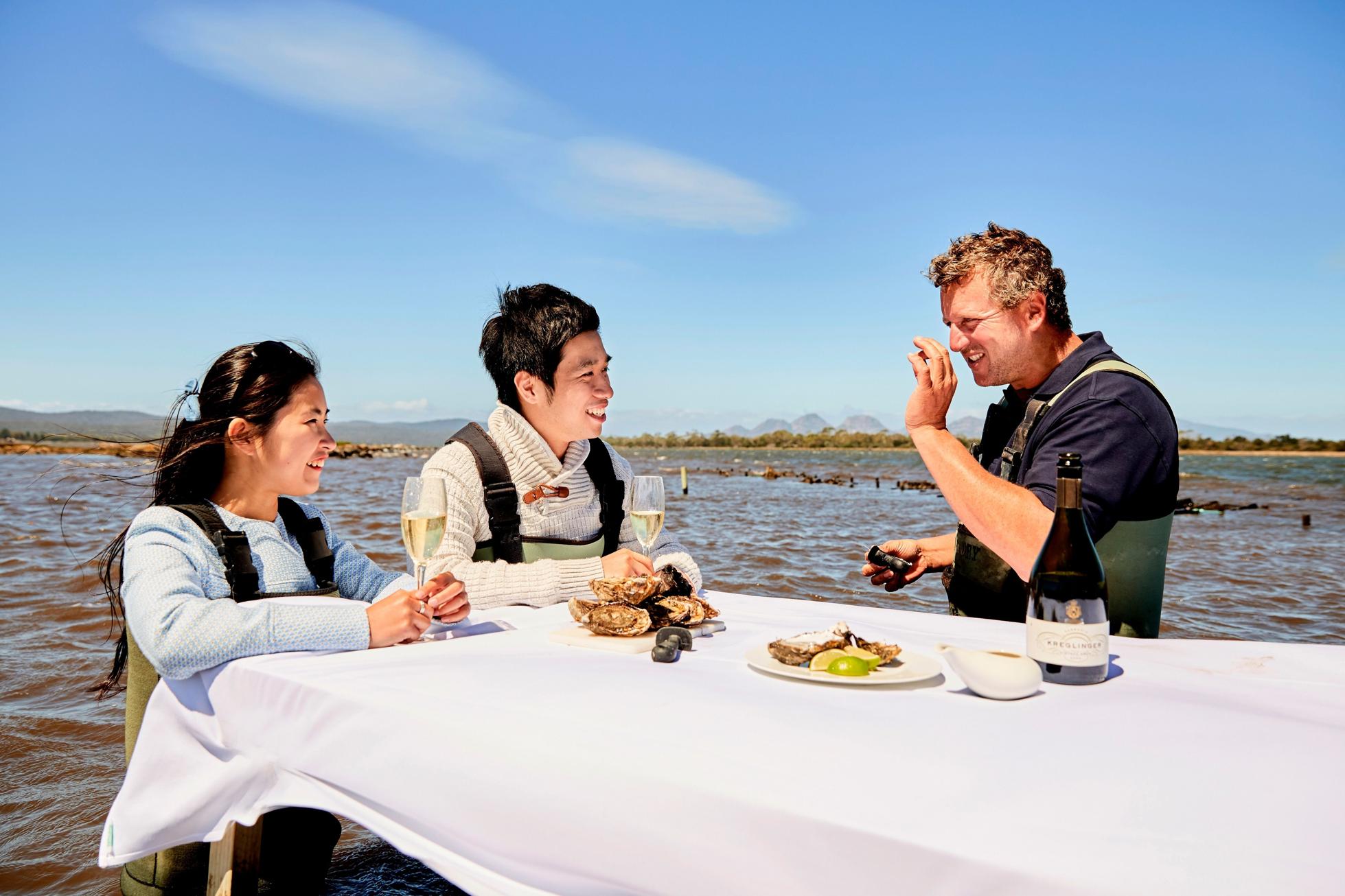 Guest wading in the waters of the Saffire Freycinet Marine farm and sampling fresh oysters