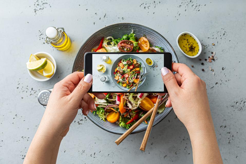 Woman taking photo of vegetable salad with smartphone. Posting food pictures (images) on social media.