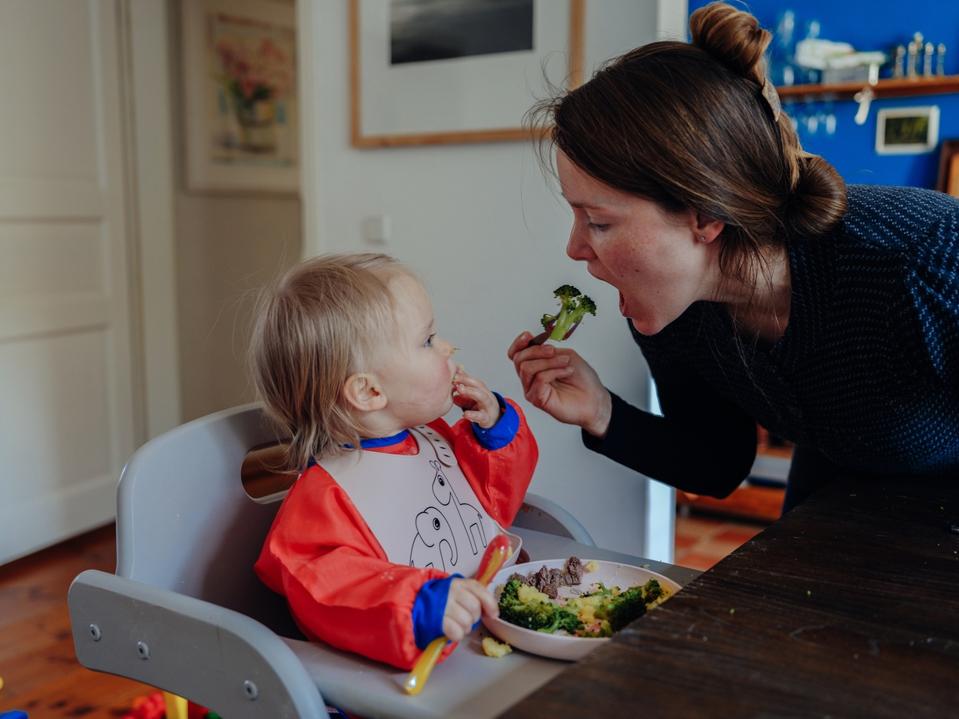 Mother eating broccoli  in front of her amazed little girl.