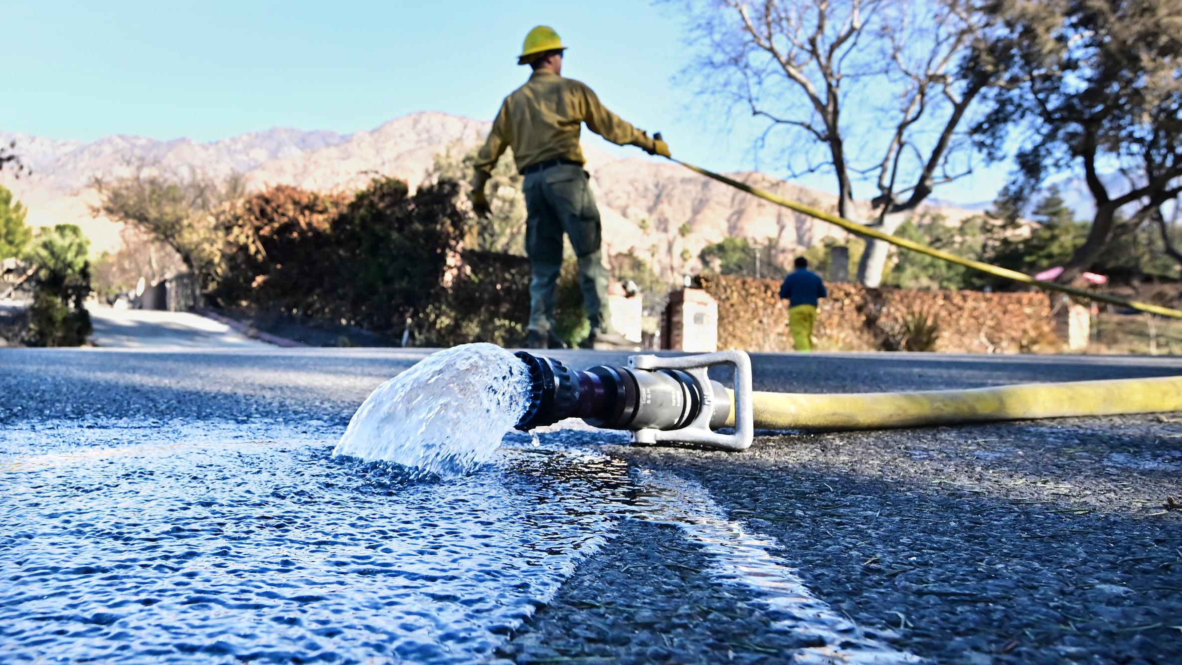 A fire hose gushes water into the street as firefighters battle wildfires in California.