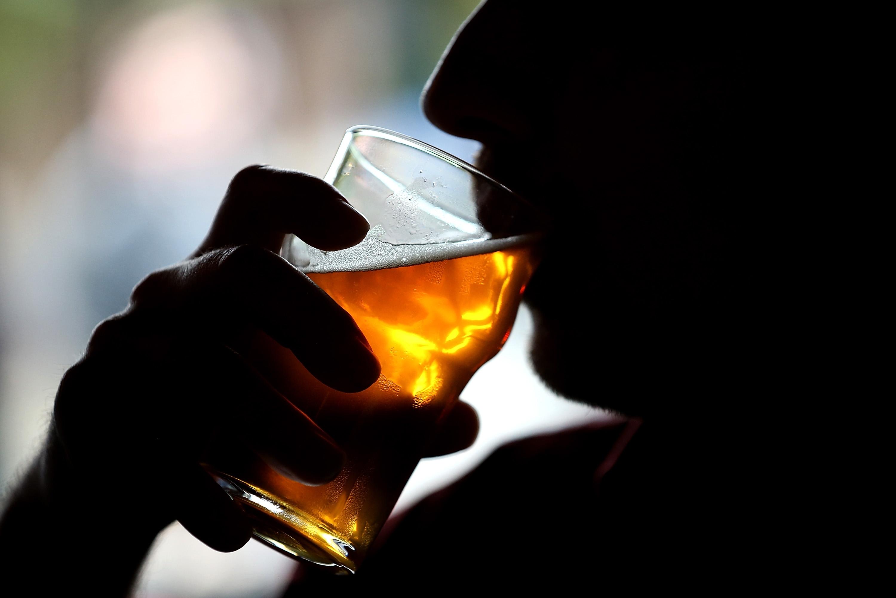 A silhouetted man raises a glass of golden beer to his lips.