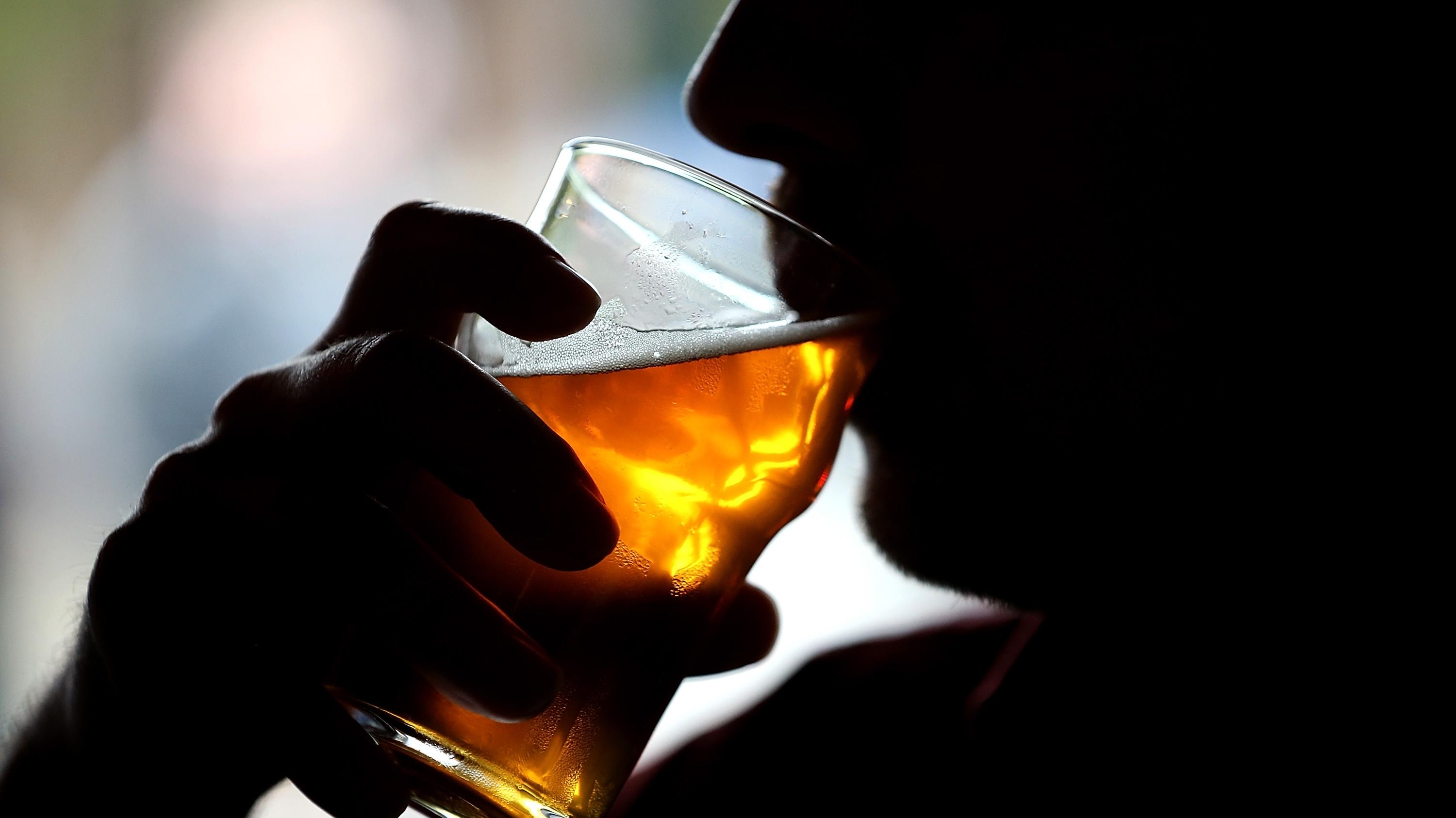 A silhouetted man raises a glass of golden beer to his lips.