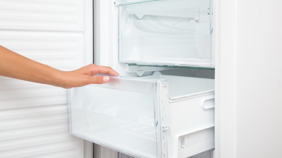 Young adult woman hand opening or closing plastic box of white freezer. Closeup. Side view.