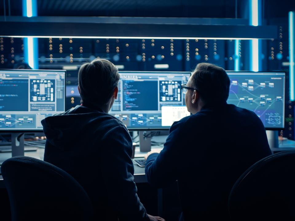 Two Professional IT Programers Discussing Blockchain Data Network Architecture Design and Development Shown on Desktop Computer Display. Working Data Center Technical Department with Server Racks