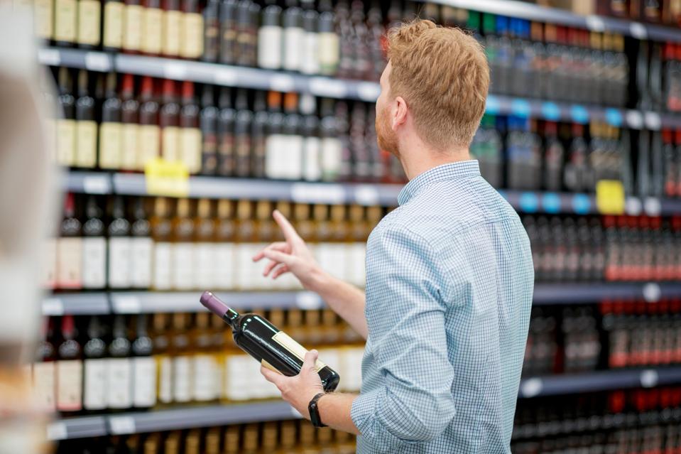 Young man holding a bottle of red wine, supermarket wine shelves