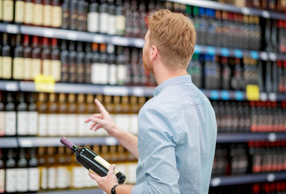 Young man holding a bottle of red wine, supermarket wine shelves