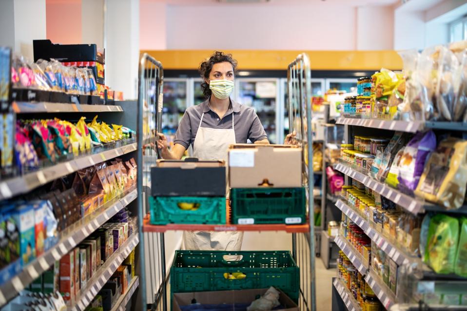 Female staff working in grocery store re-stocking goods