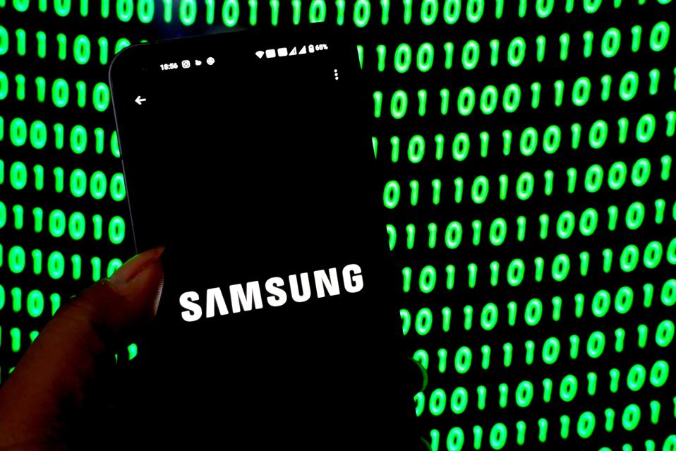 Samsung Logo seen displayed on a smartphone, green binary code in background of image.