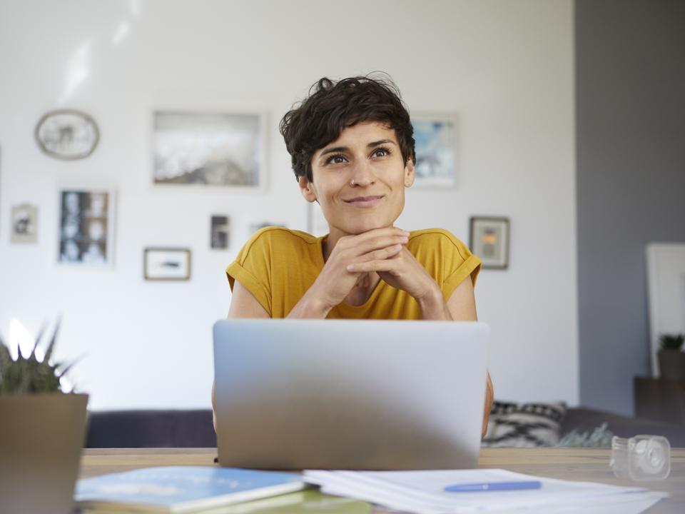 Portrait of smiling woman at home sitting at table using laptop
