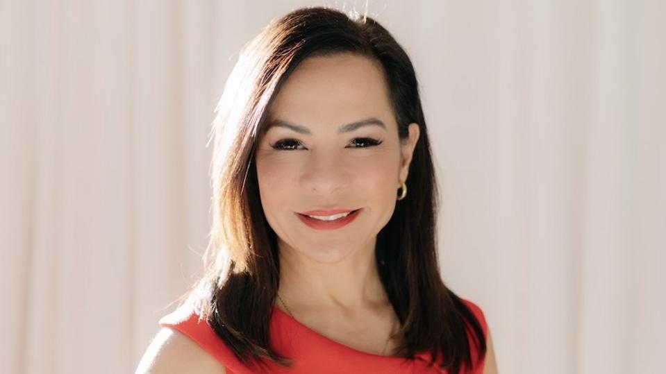 Headshot of Maria Bartolome Winans standing in front of cream curtains