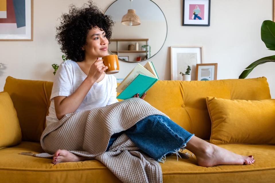 Mulher sentada no sofa com livro e xicara nas maos, mostrando um momento calmo de feriado em casa