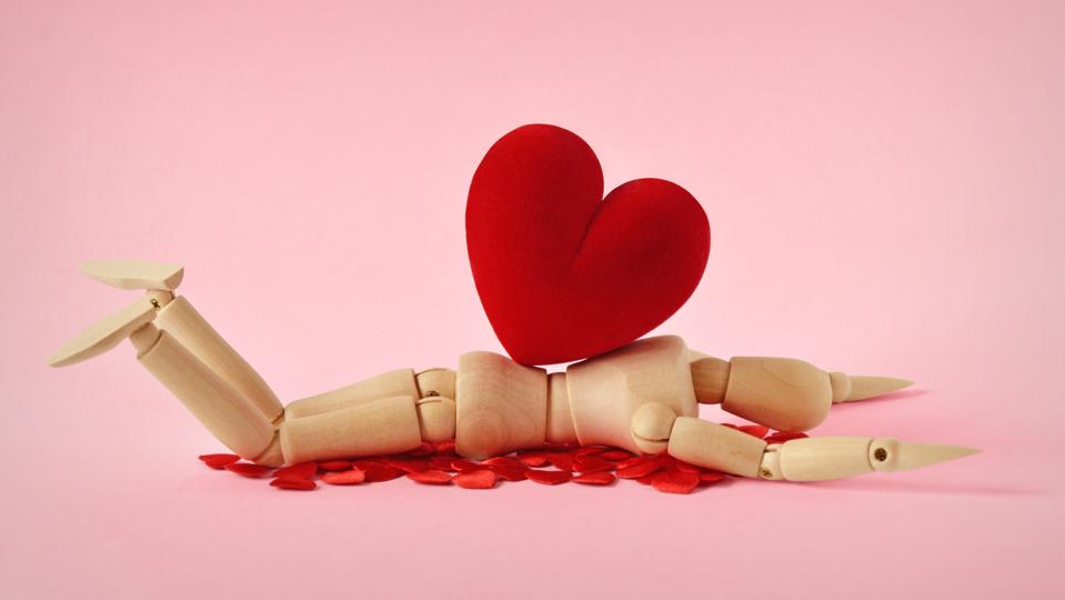 Wooden mannequin lying under heavy heart - Concept of love troubles