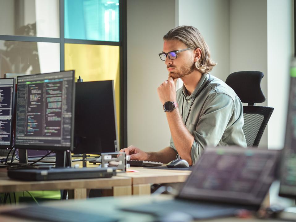 Focused Caucasian Man Coding On Desktop Computer in Stylish Office Space. Male Software Engineer Developing Innovative Application For Business Customers in Technological Start-up Company.