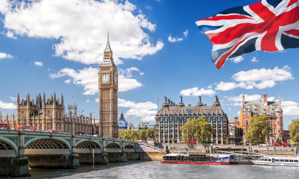 Big Ben with bridge over Thames and flag of England against blue sky in London, England, UK