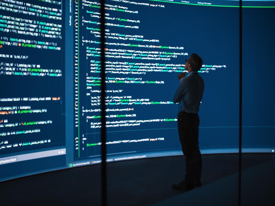 High-Tech Startup Concept: Innovative Male Software Engineer Standing, Doing Big Data Analysis on Wall Screen Showing Porgramming Code. Developing Futuristic e-Commerce App with Machine Learning.