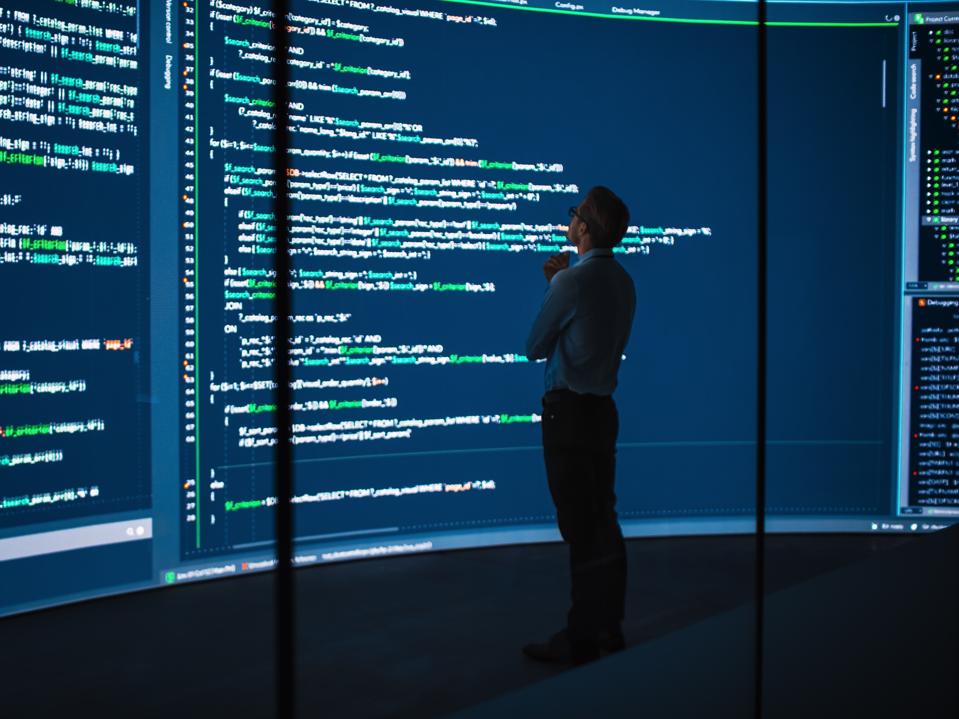 High-Tech Startup Concept: Innovative Male Software Engineer Standing, Doing Big Data Analysis on Wall Screen Showing Porgramming Code. Developing Futuristic e-Commerce App with Machine Learning.