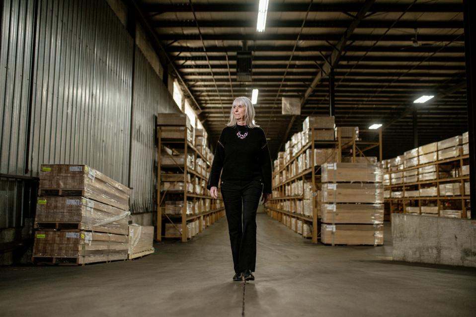 Lana Poll, older adult woman walking in a warehouse in front of shipping boxes and crates