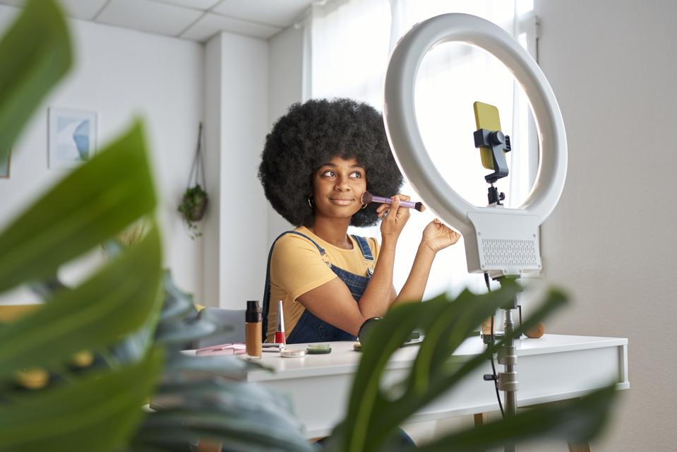 Beauty blogger using a mobile phone while recording a makeup tutorial for her social networks.