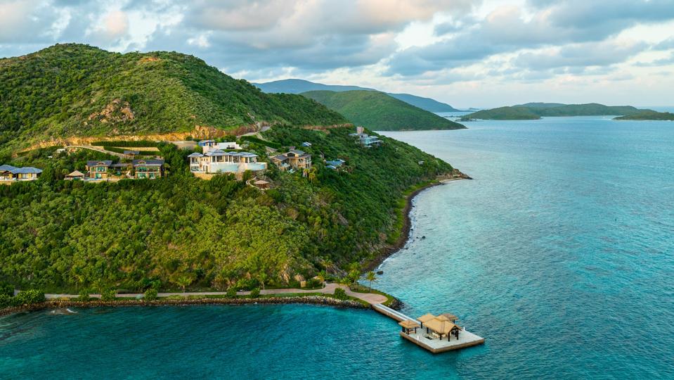 An overhead shot of a tall, forested hill that's covered in cliffside villas with a port below