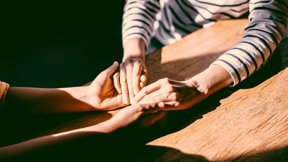 Two unrecognizable persons holding each other's hands. Emotional support during hard times
