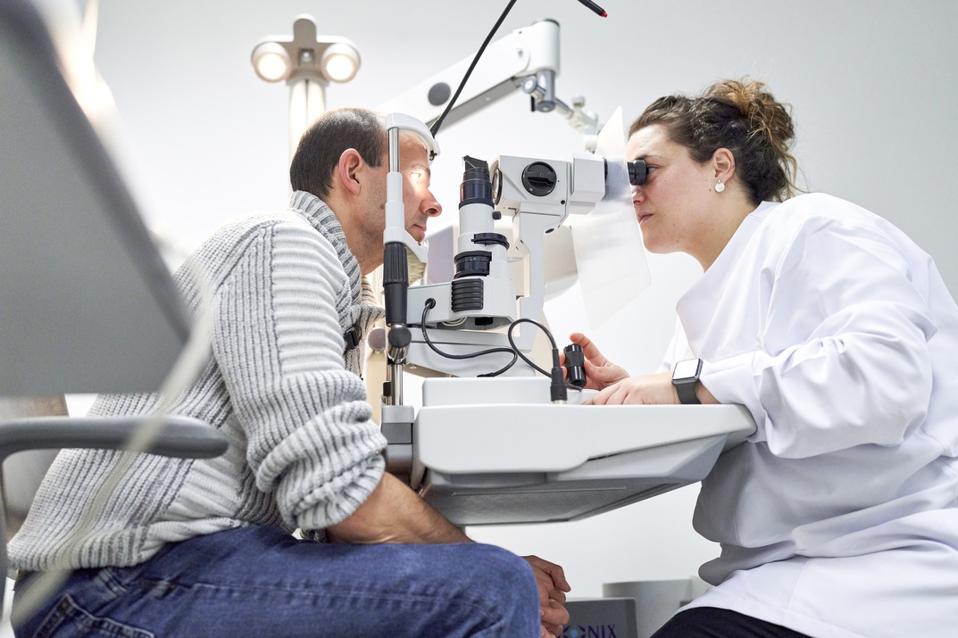 Female ophthalmologist examining male patient in ophthalmology clinic with autorefractometer, examination of eyesight.