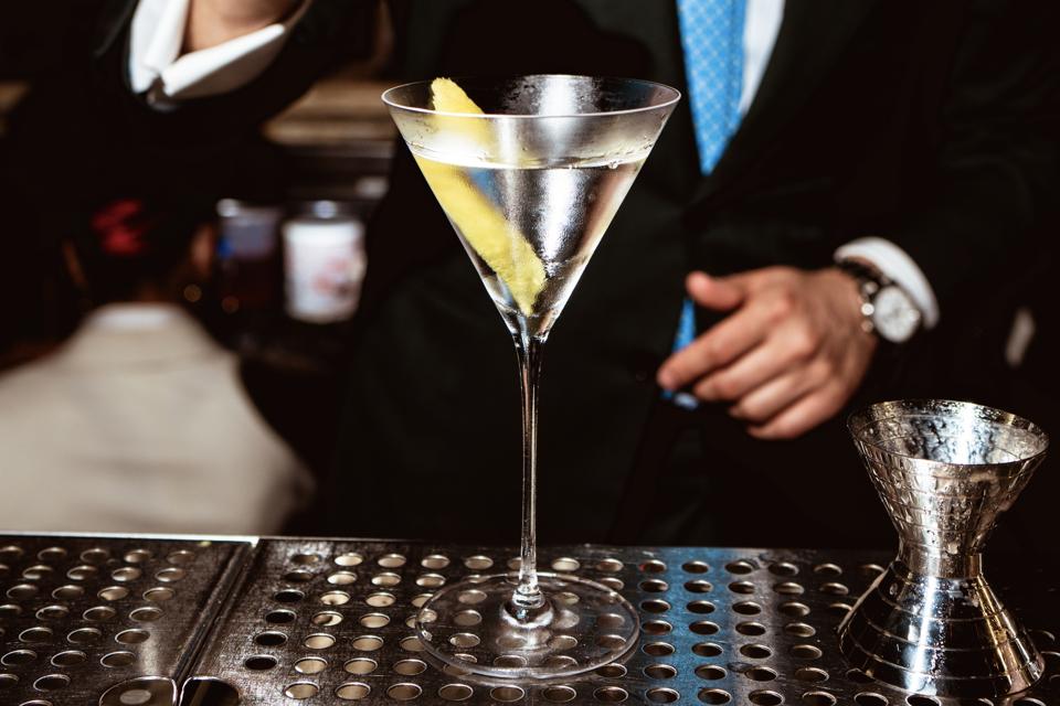 Vodka In martini glass with lemon twist on metal bar with bartender.