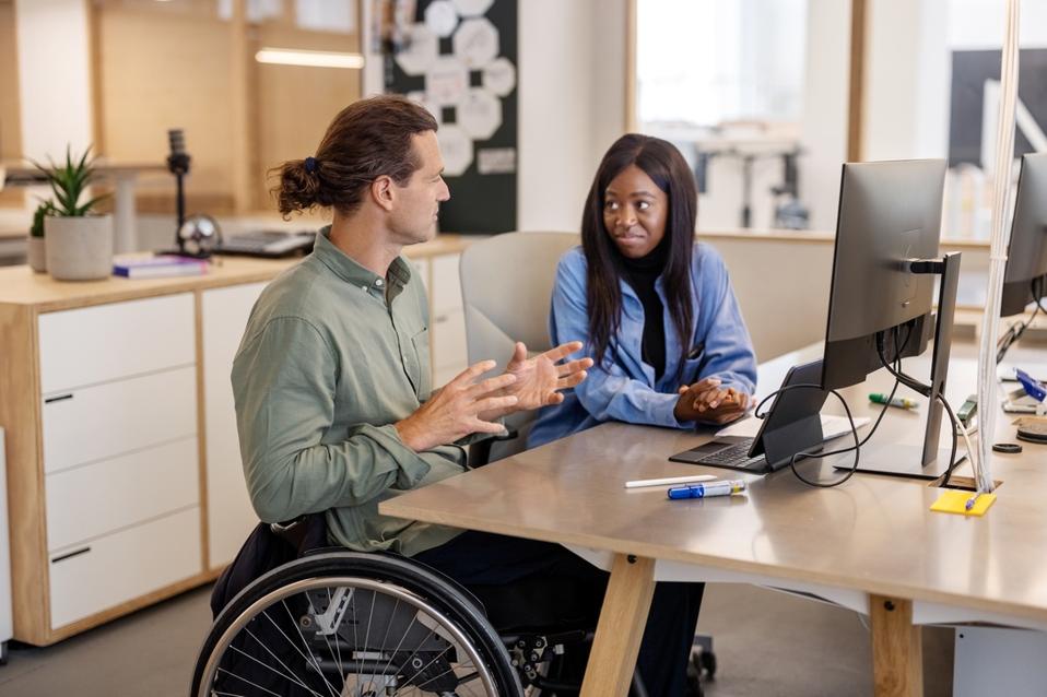 Mature businessman in wheelchair talking with woman colleague at office