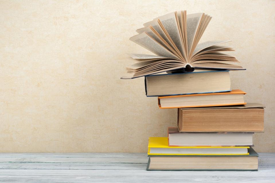 Stack of colorful books on gray wooden table with cream white wall in the background. 