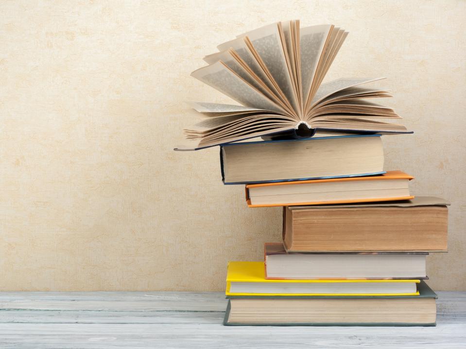 Stack of colorful books on gray wooden table with cream white wall in the background.