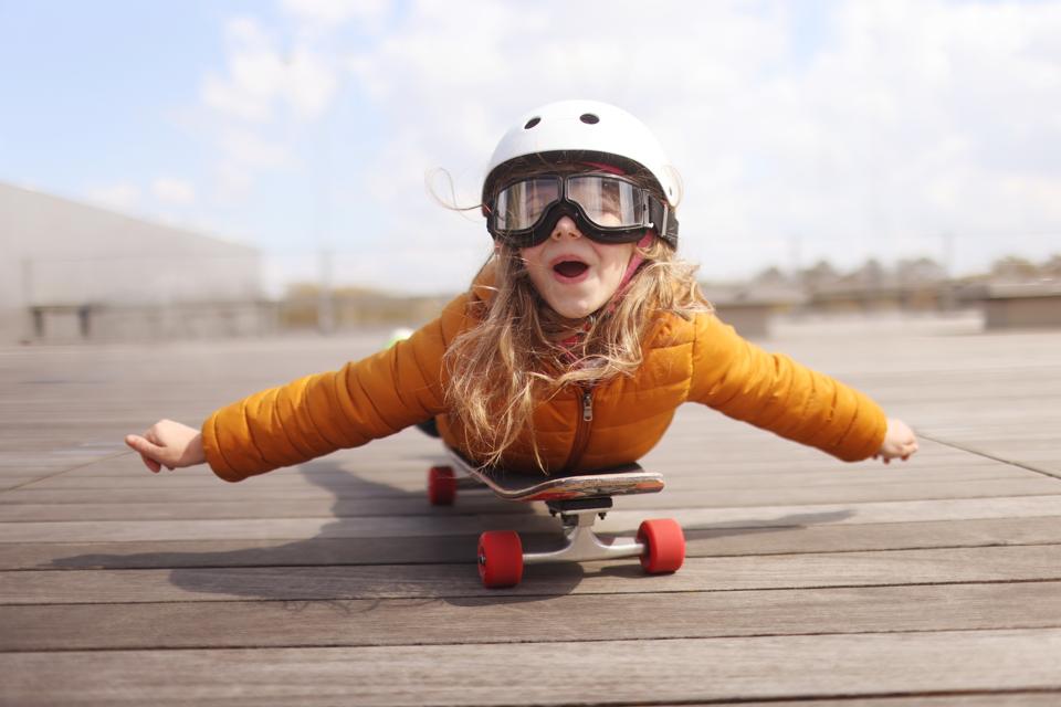 A young girl laying on a skateboard, seeming to fly