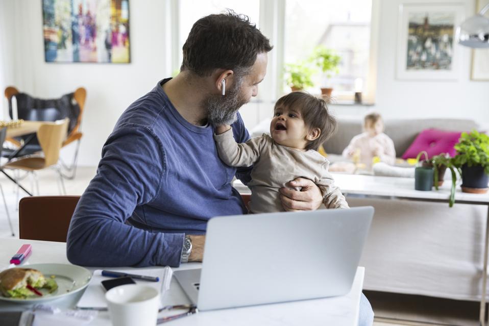 Smiling baby boy with working father in living room at home
