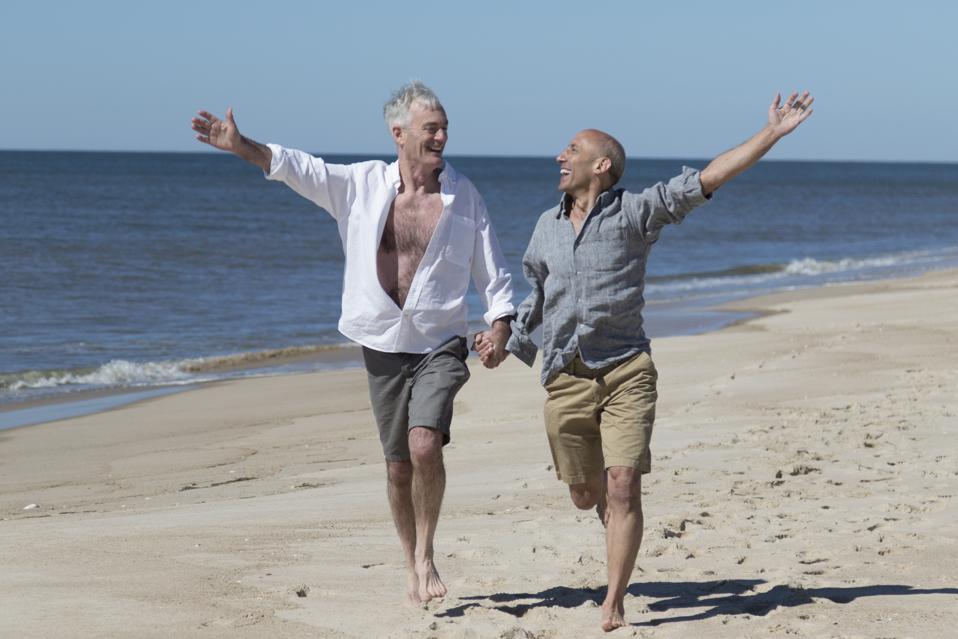Pareja gay senior tomados de la mano y corriendo con alegría en la playa