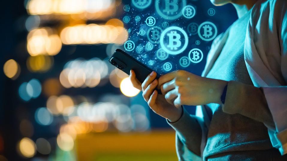 Mid-section of young Asian woman using smartphone in city at night, against illuminated street lights bokeh, working with Bitcoin technologies, investing or trading Bitcoin on cryptocurrency. Business on the go