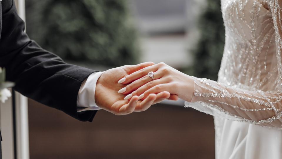 The man gently holds the bride's hand with a beautiful golden wedding ring. Enlarged image of newlyweds' hands. Wedding concept. The groom gently touches the bride