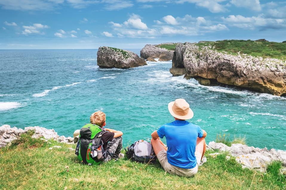 Father and son backpacker pilgrims rest on the rocky sea side and enjoy beautiful view