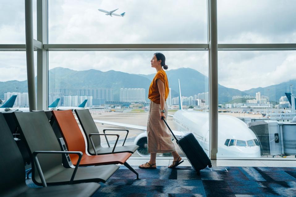 Jeune femme asiatique portant une valise, marchant près de la fenêtre au terminal de l'aéroport. Jeune femme voyageuse asiatique en attente d'embarquement à l'aéroport. Voyage d'affaires. Concept de voyage et de vacances