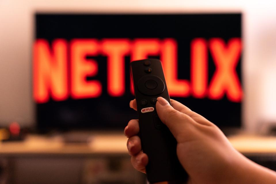 A hand holding a tv remote with a Netflix logo on a tv screen 