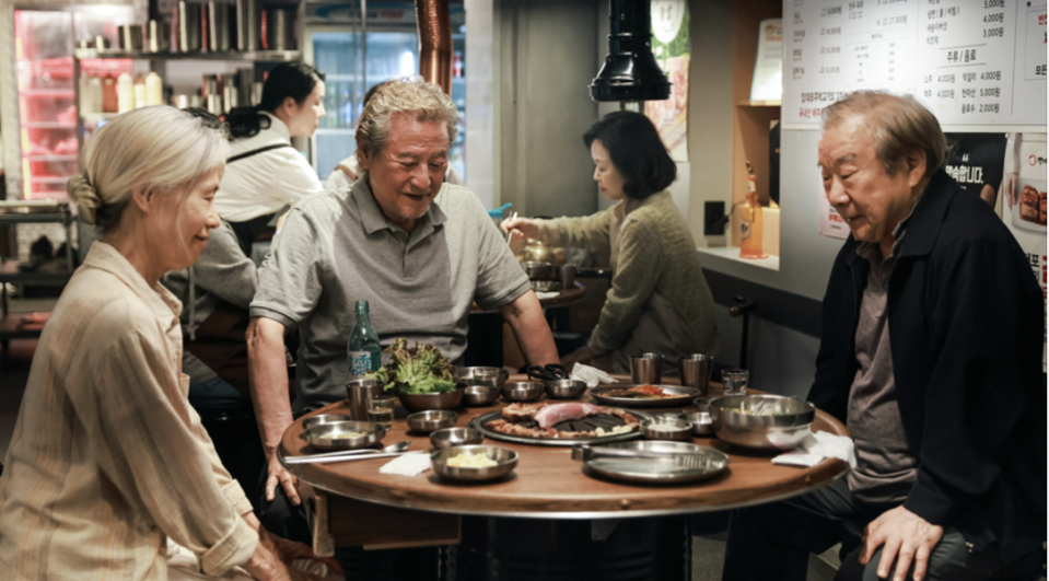 Two older Korean men and one older Korean woman sit around a table in a restaurant.